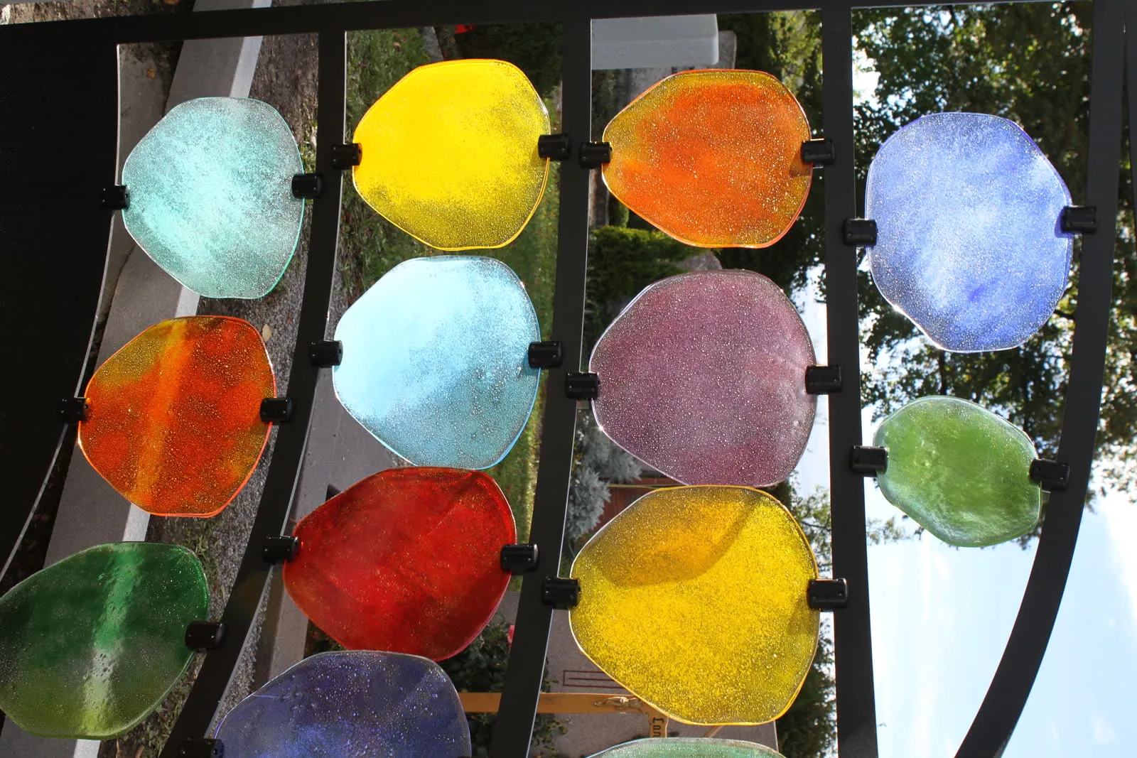 Gelbe, rote, türkise und violette Glasscheiben leuchten im Gegenlicht im schwarzen Stahlrahmen – STOI Steinmetzwerkstatt